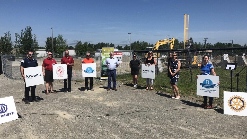 Huit personnes posent côte à côte à deux mètres de distance, certains tenant des affiches du Club Kiwanis ou Richelieu.