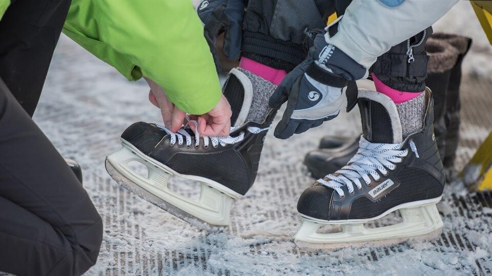Une personne en aide une autre à chausser ses patins.