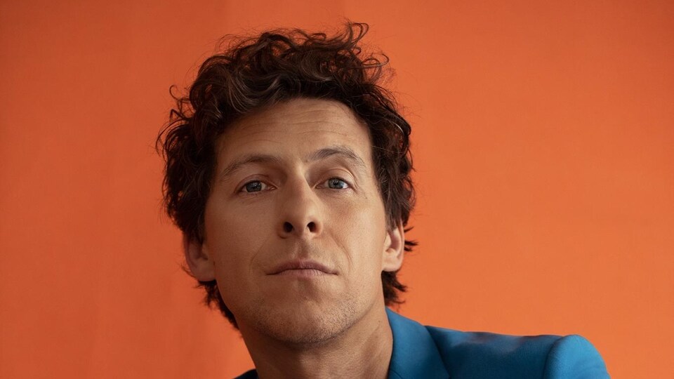 Un homme dans un veston bleu sur fond orange.