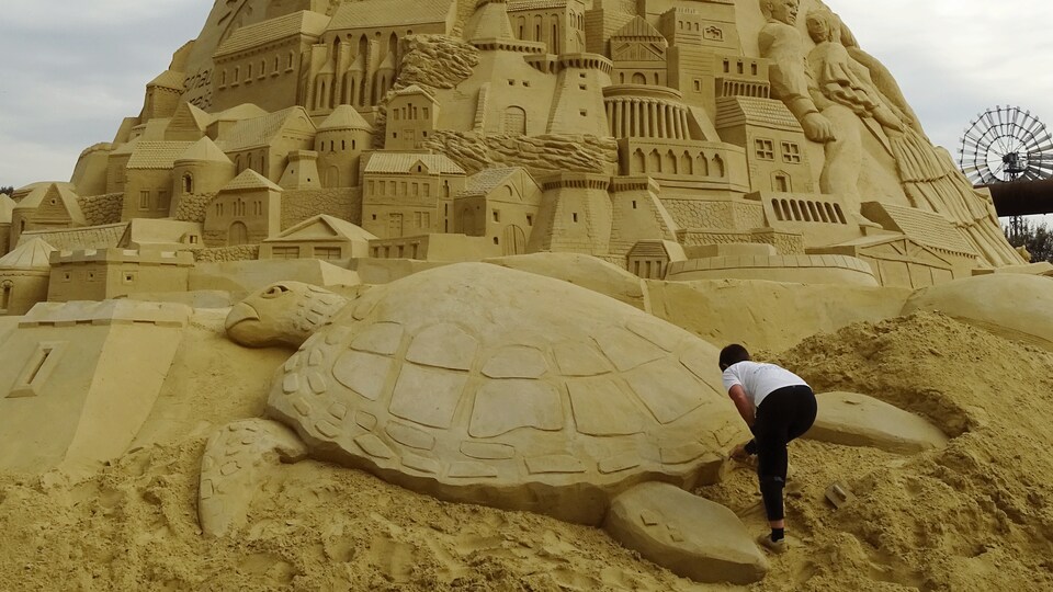 La sculptrice Patricia Leguen ajoute des détails à une sculpture d'une tortue en sable. En 2017 en Allemagne, elle fait partie d'une équipe qui établira le nouveau record Guinness pour le plus haut château de sable.