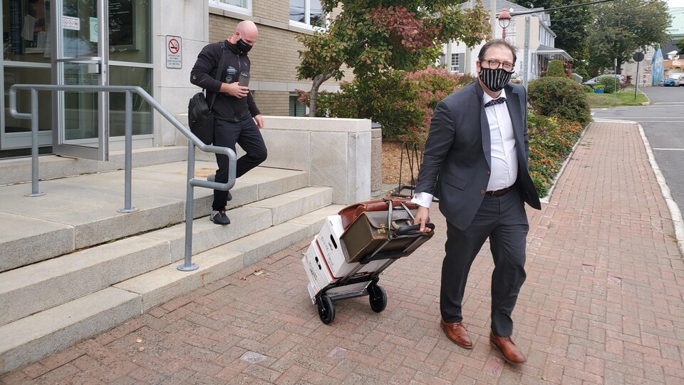 Patrick Chénard descend les marches du palais de justice pendant que, devant lui, sur le trottoir, son avocat, Yves Desaulniers, tire des boîtes de documents sur un petit chariot.
