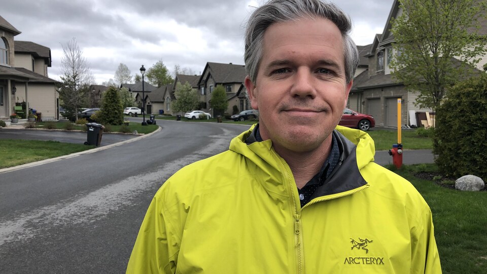 Un homme se laisse prendre en photo à l'extérieur, dans un quartier résidentiel.