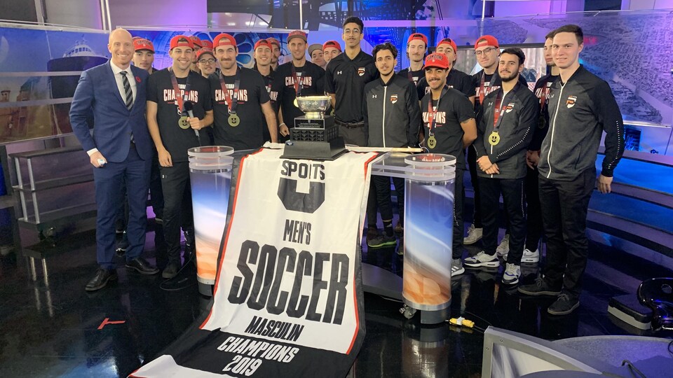 L'équipe sur le plateau avec le trophée et la banderole de la victoire.