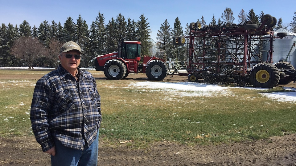 Un homme en avant-plan devant un tracteur au printemps