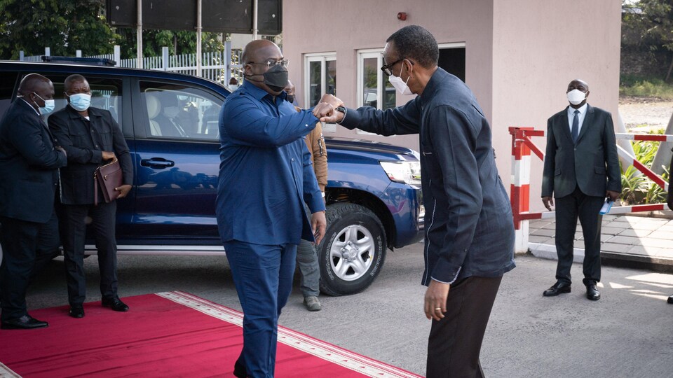 Les deux hommes se saluent du coude sur un tapis rouge.