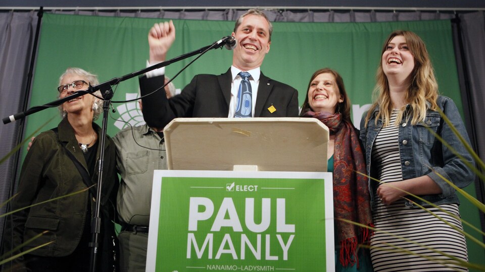 Accompagné de membres de sa famille, Paul Manly s'adresse au micro, le sourire aux lèvres et le poing levé en signe de victoire.