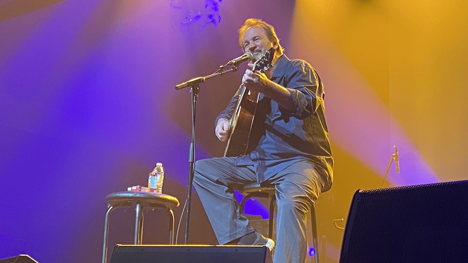 Le chanteur assis sur un banc chante et joue de la guitare. 