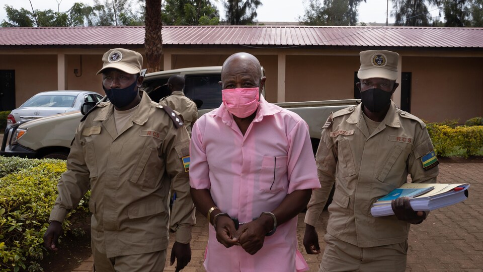 Paul Rusesabagina menotté, escorté par deux policiers. 
