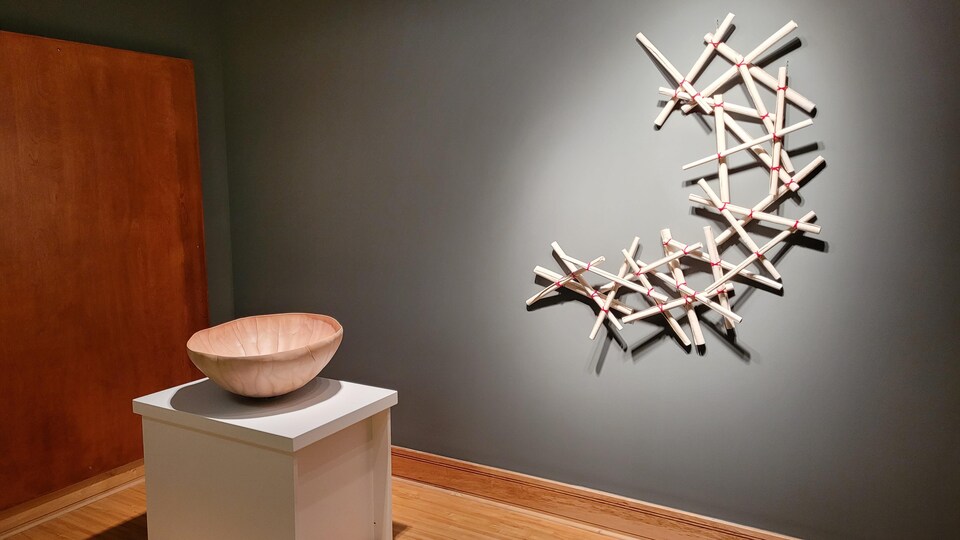 Les rouleaux de céramique sont fixés au mur, alors que le bol aux nuances de beige est exposé sur un socle blanc.