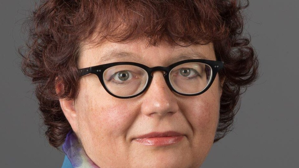 Femme aux cheveux courts noirs et bouclés, portant des lunettes de vue noires.