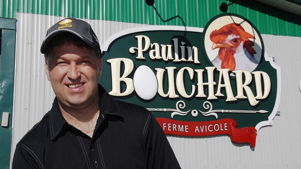 Paulin Bouchard devant le logo de sa ferme qui porte son nom.