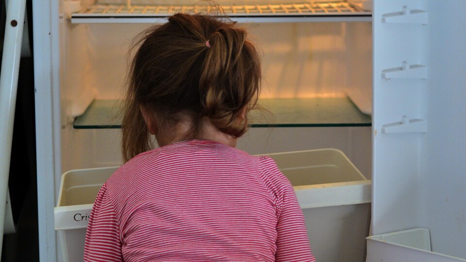 Une fillette assise devant un frigo vide.