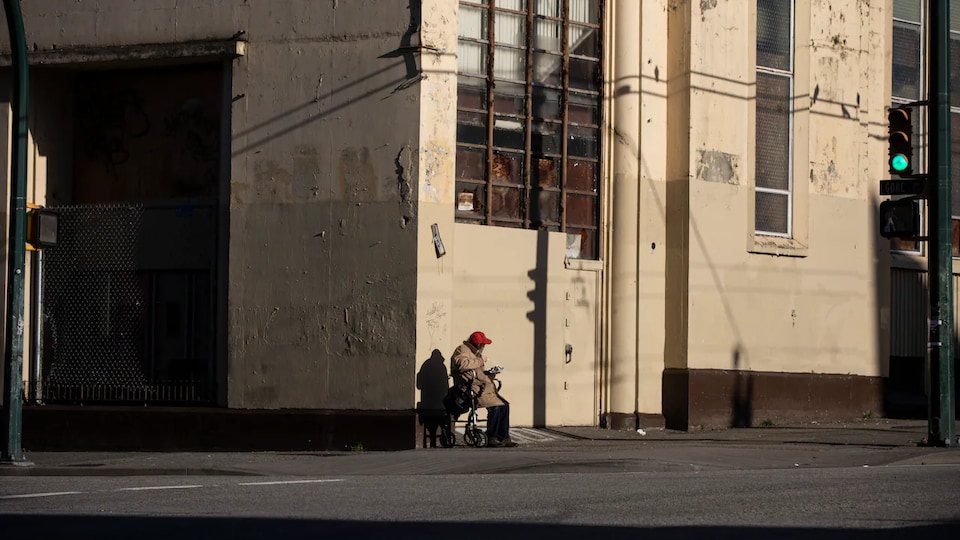 Un homme âgé assi sur un fauteuil roulant mange son repas de midi au coin d'une rue déserte à Vancouver en décembre 2020.