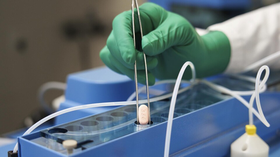 Dans un laboratoire, un chercheur tient une pilule dans une pince.