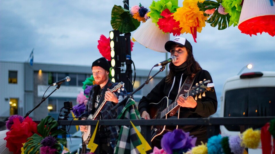 Sara Dufour et un musicien chantent dans une remorque décorée aux couleurs festives.