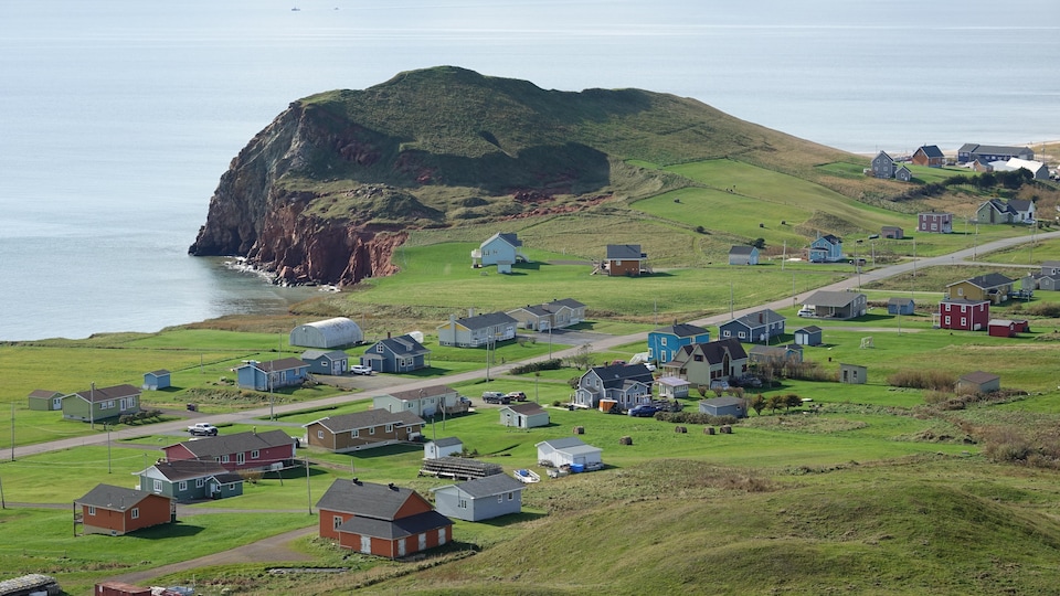 Des maisons dans un paysage verdoyant avec une butte rocheuse en arrière-plan.