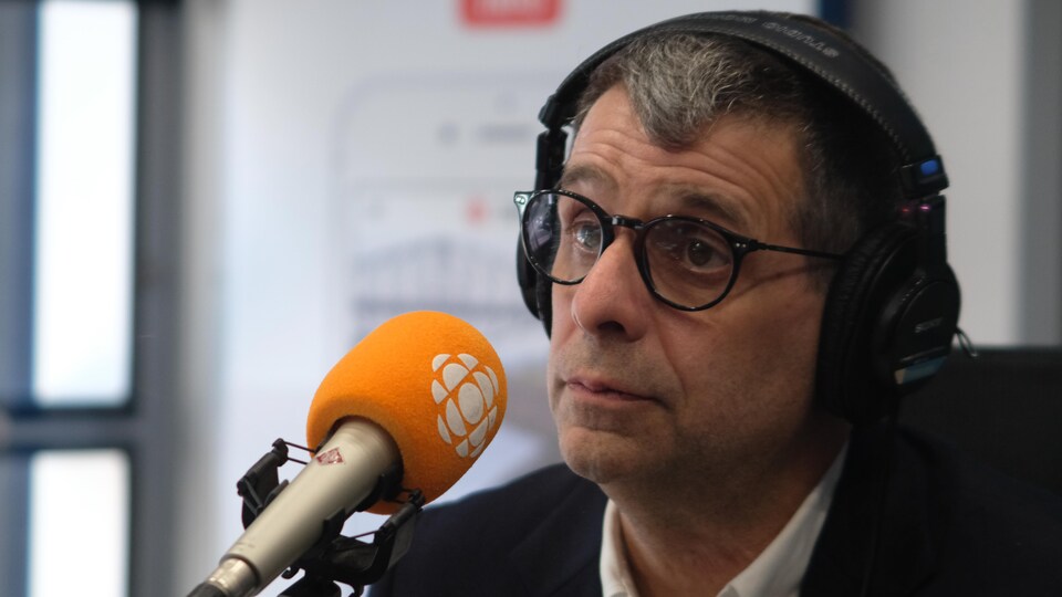 Un homme avec des lunettes derrière un micro dans un studio de radio.