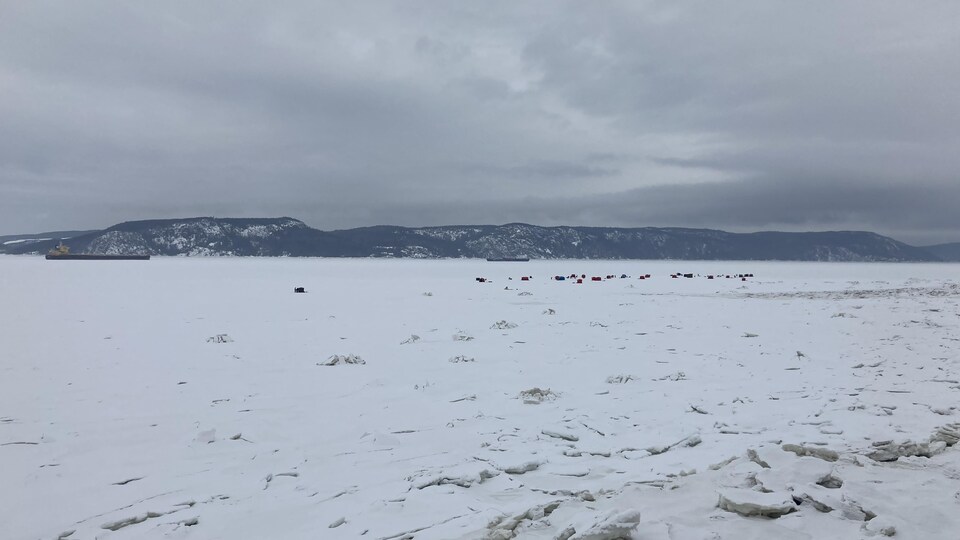 Une baie glacée avec au loin des tentes et un navire.