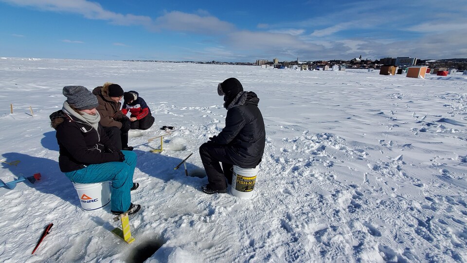 Des amateurs de pêche sur glace patientent devant leurs trous.