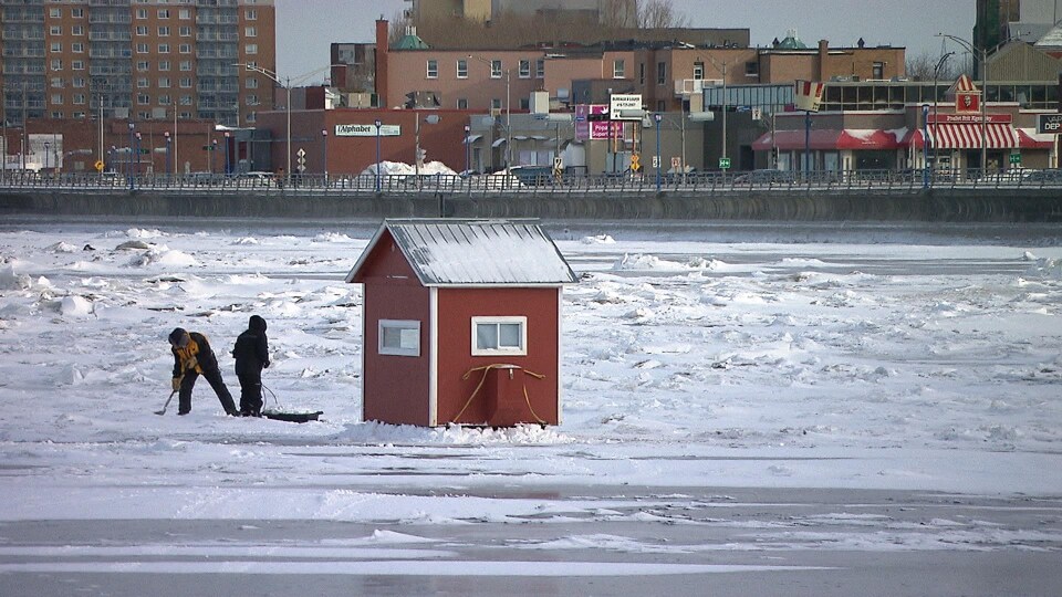 Deux personnes installent leur cabane sur la banquise, face au centre-ville de Rimouski.