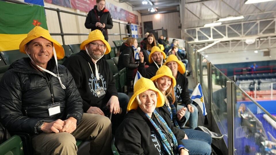 Des amateurs de curling avec des chapeaux de pêche jaunes sur la tête.