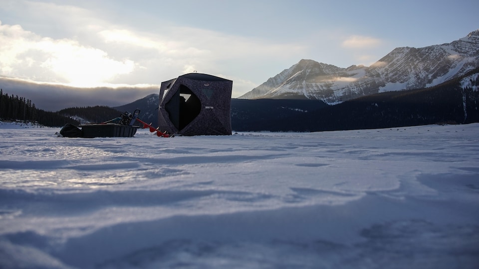Une tente est installée sur le lac Upper Kananaskis. Un traîneau chargé de matériel est placé à côte.