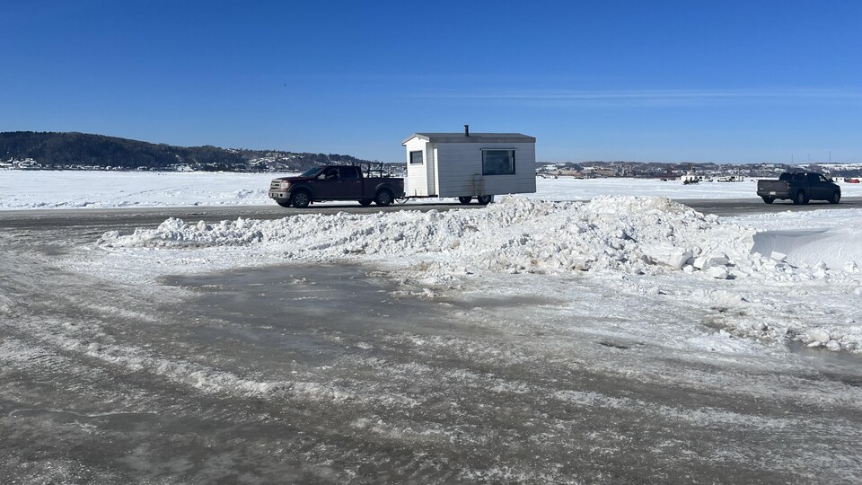 Une camionnette qui tire une cabane de pêche blanche et qui se dirige vers le pont de glace du village de pêche blanche.