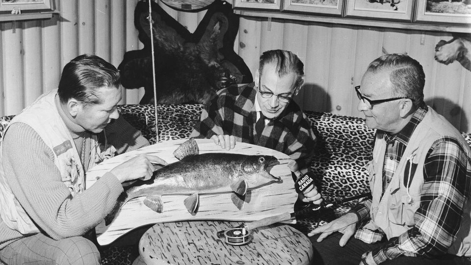 Dans une pièce remplie d'objets associés à la chasse et la pêche dont un poisson naturalisé, l'animateur Serge Deyglun, le
réalisateur Marc Perron et l'animateur Richmond Pelletier, discutent autour d'une table.