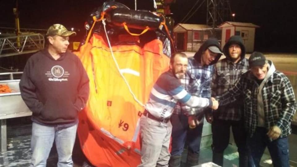 Cinq hommes se trouvent au port de Grande-Rivière devant un canot de sauvetage.