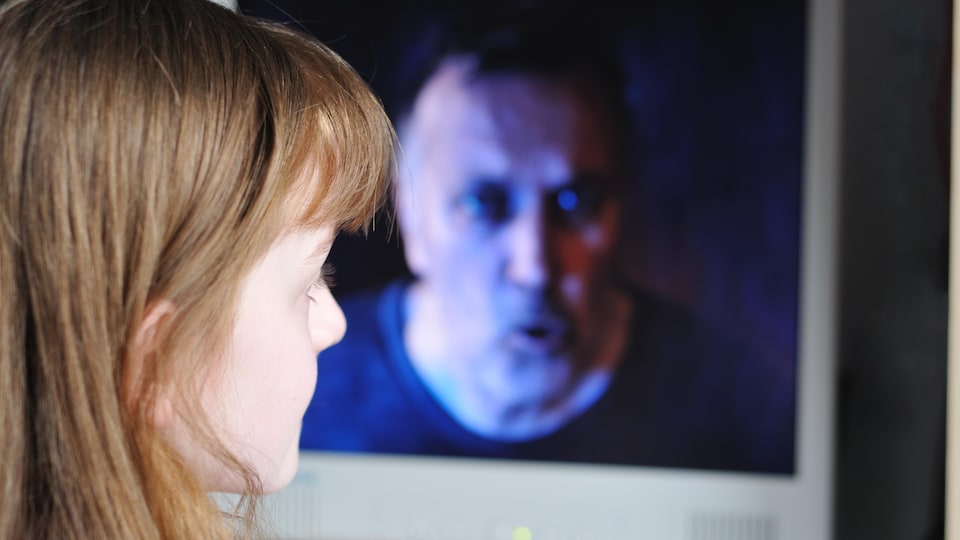 Une enfant regarde un homme menaçant sur un écran d'ordinateur.