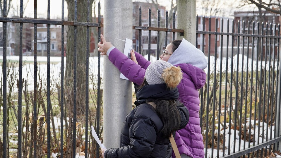 Deux personnes posent une affiche sur un lampadaire.