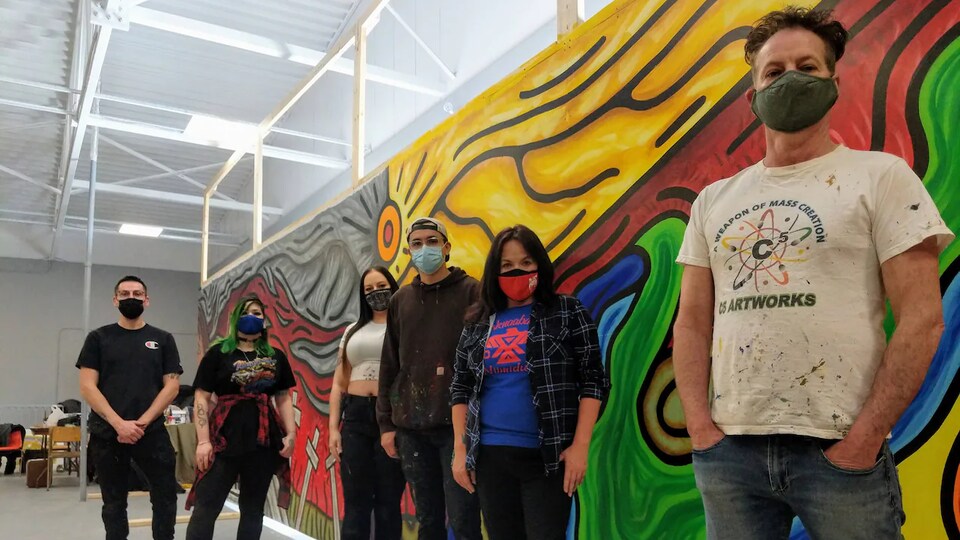 Des gens posent devant une peinture sur un mur.