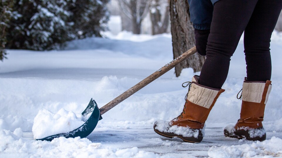 Le bas du corps d'une personne qui pellette de la neige avec une pelle.