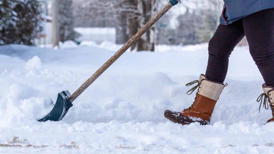 Le bas du corps d'une personne qui pellette de la neige avec une pelle.