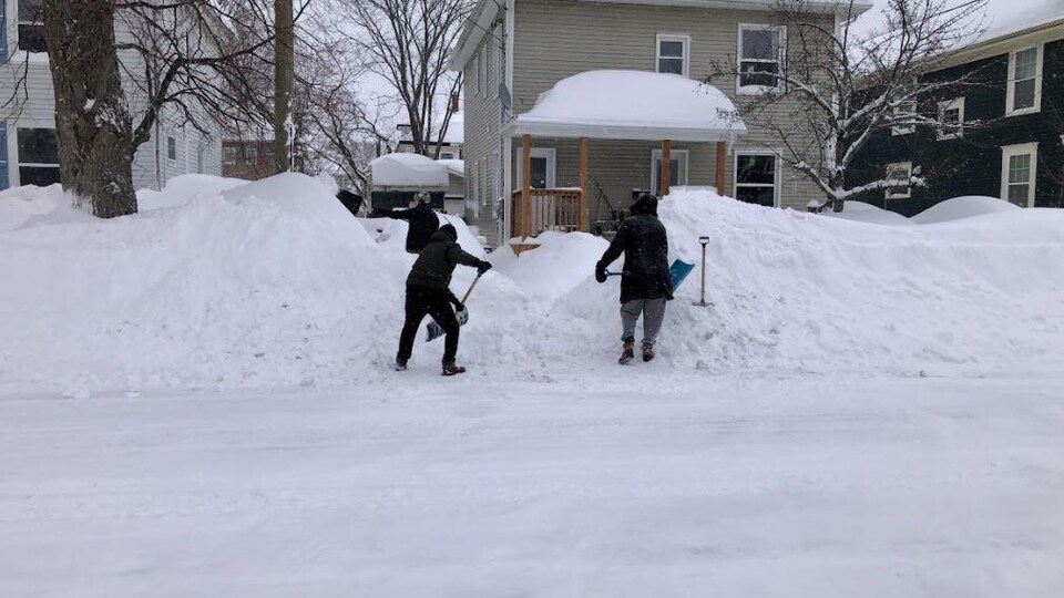 Deux personnes pellettent de la neige. 