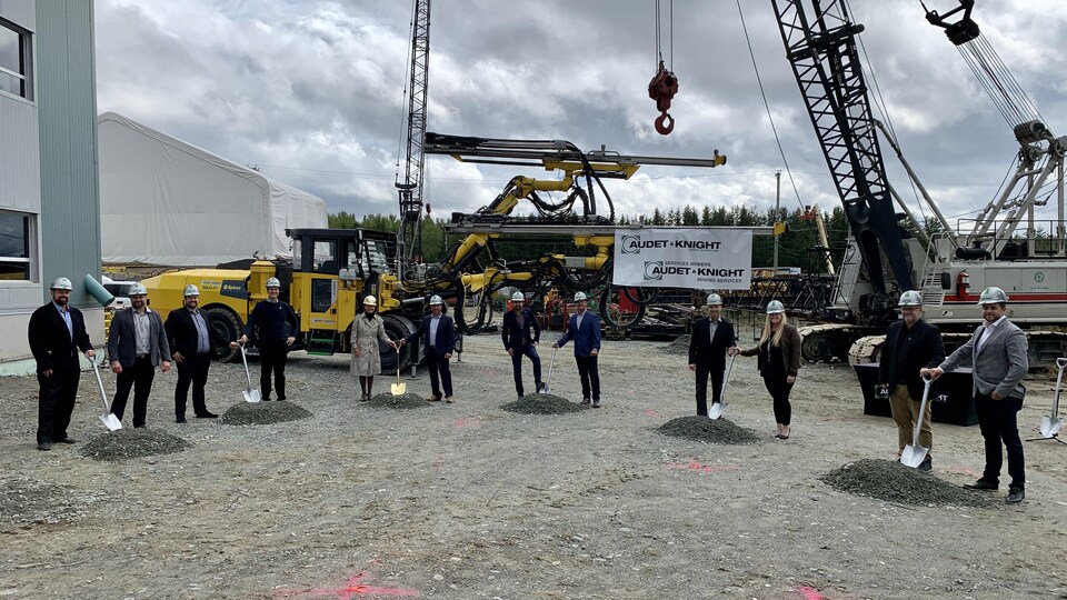 12 personnes tiennent une pelle devant de la machinerie.