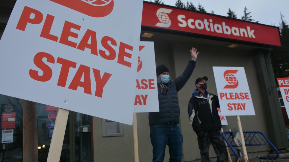 Des gens tiennent des pancartes devant une Banque Scotia.