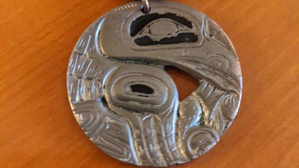 Un pendentif rond en étain représentant une tête de corbeau.