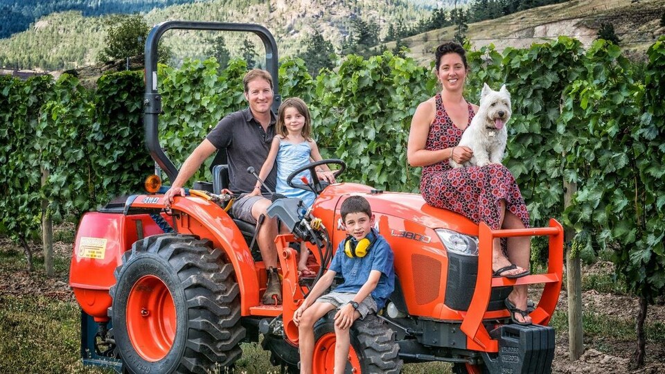 une famille de trois enfants sur un tracteur, la femme a un chien sur les genous, avec la vigne en fond.
