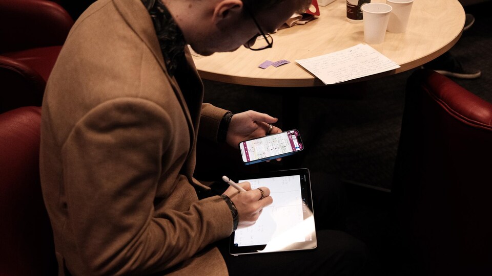 Un homme, concentré, prend des notes sur son iPad dans les loges de la Place Bell. 