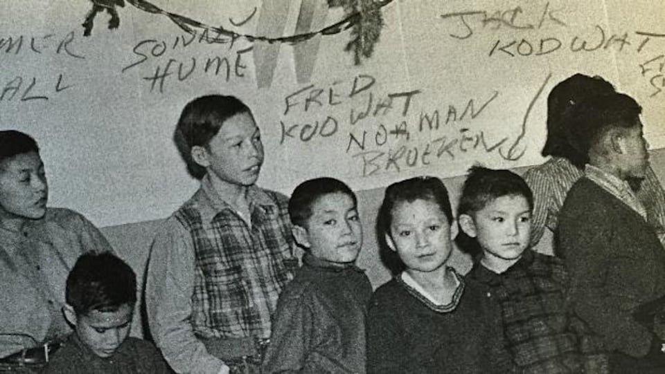 Des enfants du pensionnat autochtone Baptist Mission School sont debout devant un mur un jour de Noël à Whitehorse.