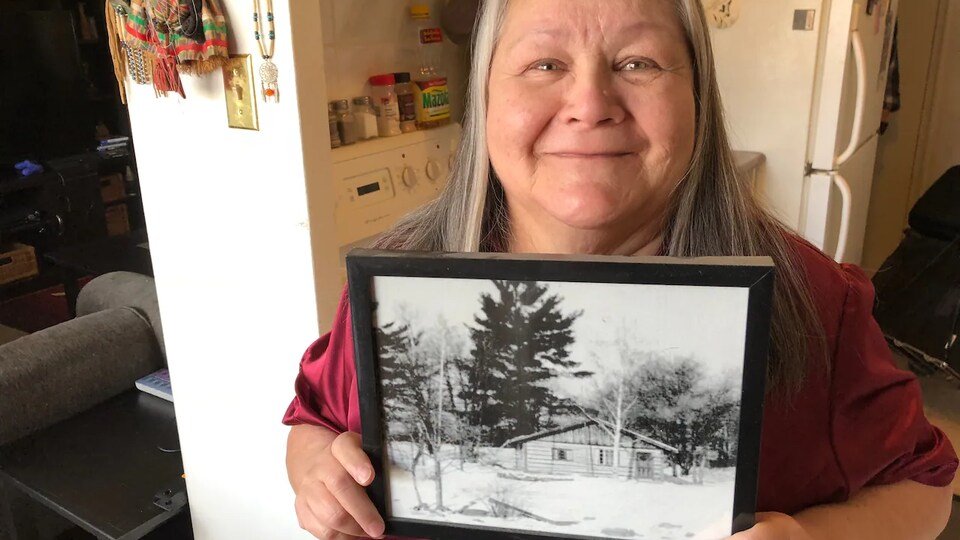 Portrait de Karen Chaboyer qui tient dans ses mains une photo d'une maison en bois.