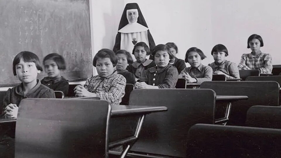 Un groupe d'élèves et une religieuse posent dans une salle de classe du pensionnat pour Autochtones de Cross Lake, au Manitoba.