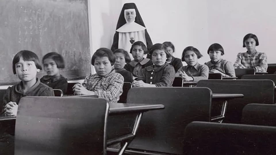 Un groupe d'étudiantes et une religieuse posent dans une salle de classe du pensionnat pour Autochtones.