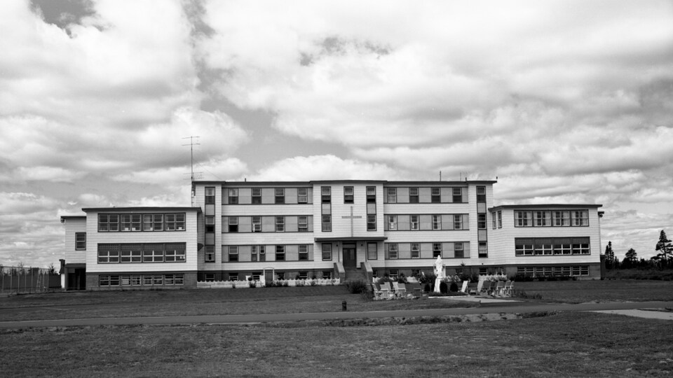 Une photo en noir et blanc du pensionnat, un bâtiment en forme de croix sur un grand terrain de gazon.