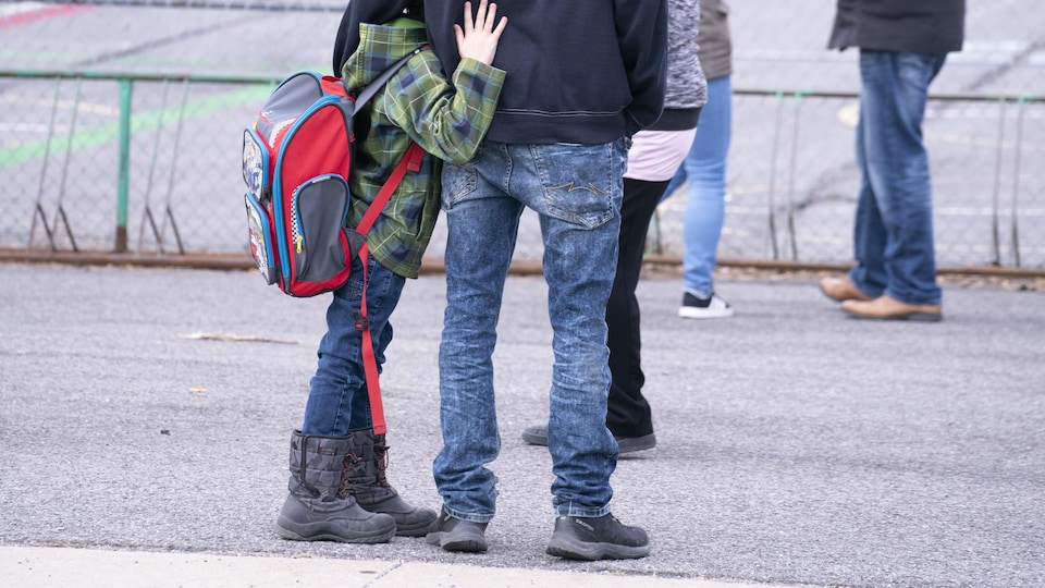 Un enfant enlace son père dans la cour d'école.