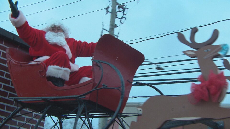 Le père Noël salue les gens depuis son traîneau monté sur un char allégorique.