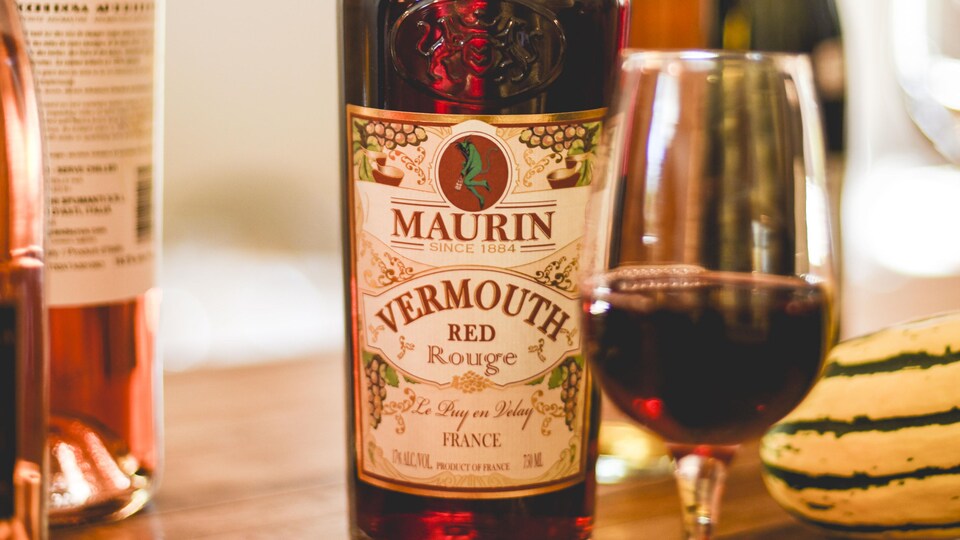 Une bouteille de vermouth, un verre de rouge. Une courge, et d'autres bouteilles en arrière-plan sur la table.