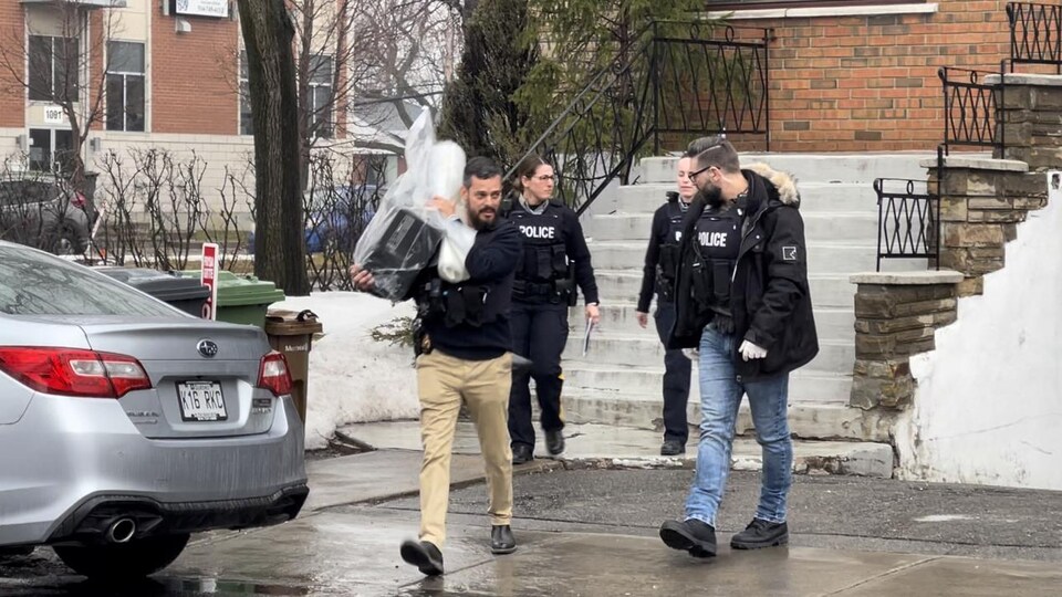 Un enquêteur transporte un ordinateur à la sortie d'une résidence.
