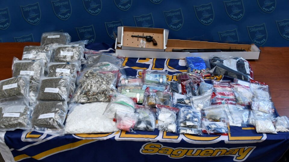De la drogue en sacs et des armes sur une table.